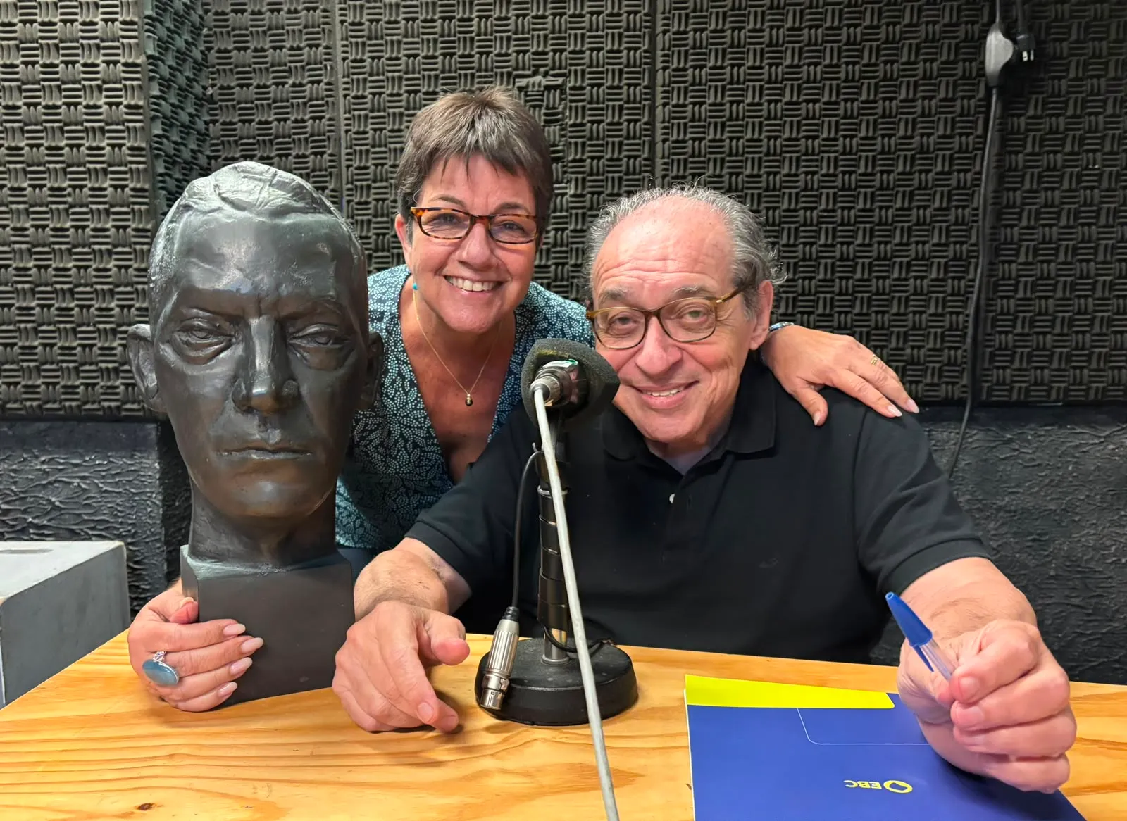 Heloisa Seixas e Ruy Castro no estúdio da Rádio MEC, com um microfone e um busto de bronze